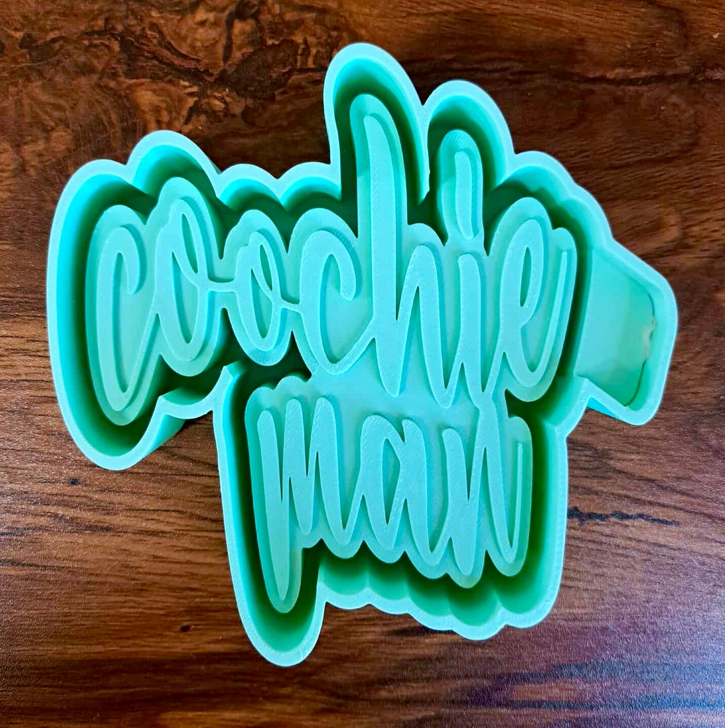 Green 3D housing with 'coochie man' text on a wooden surface used to make silicone molds