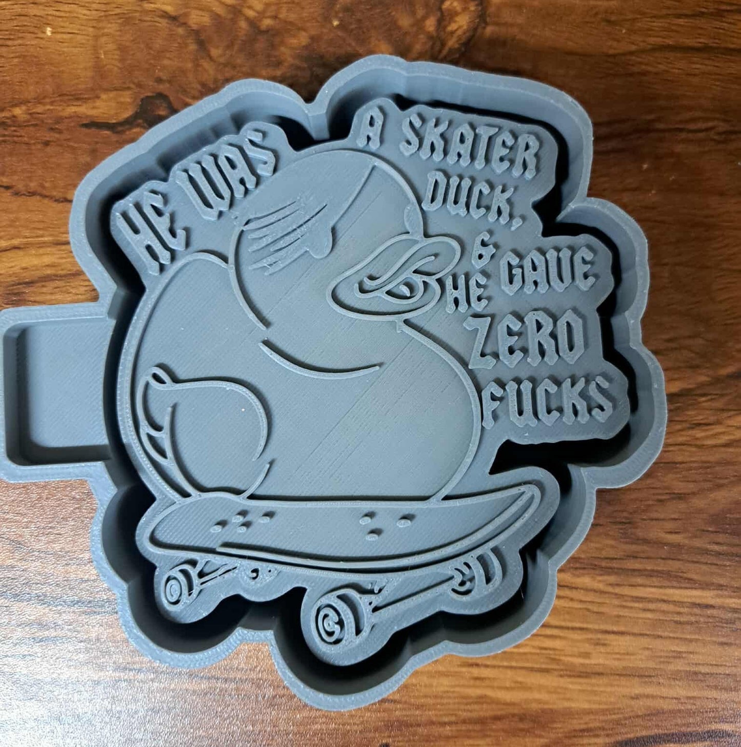 Gray mold housing with duck design and text on a wooden surface used to sell silicone molds