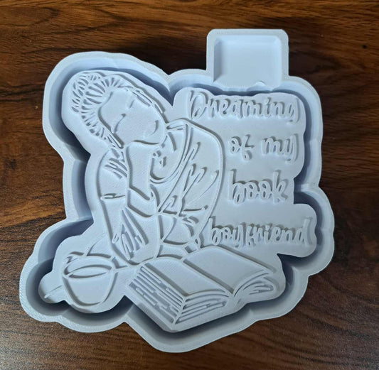 Silicone mold housing with a design of a person reading a book, on a wooden surface.
