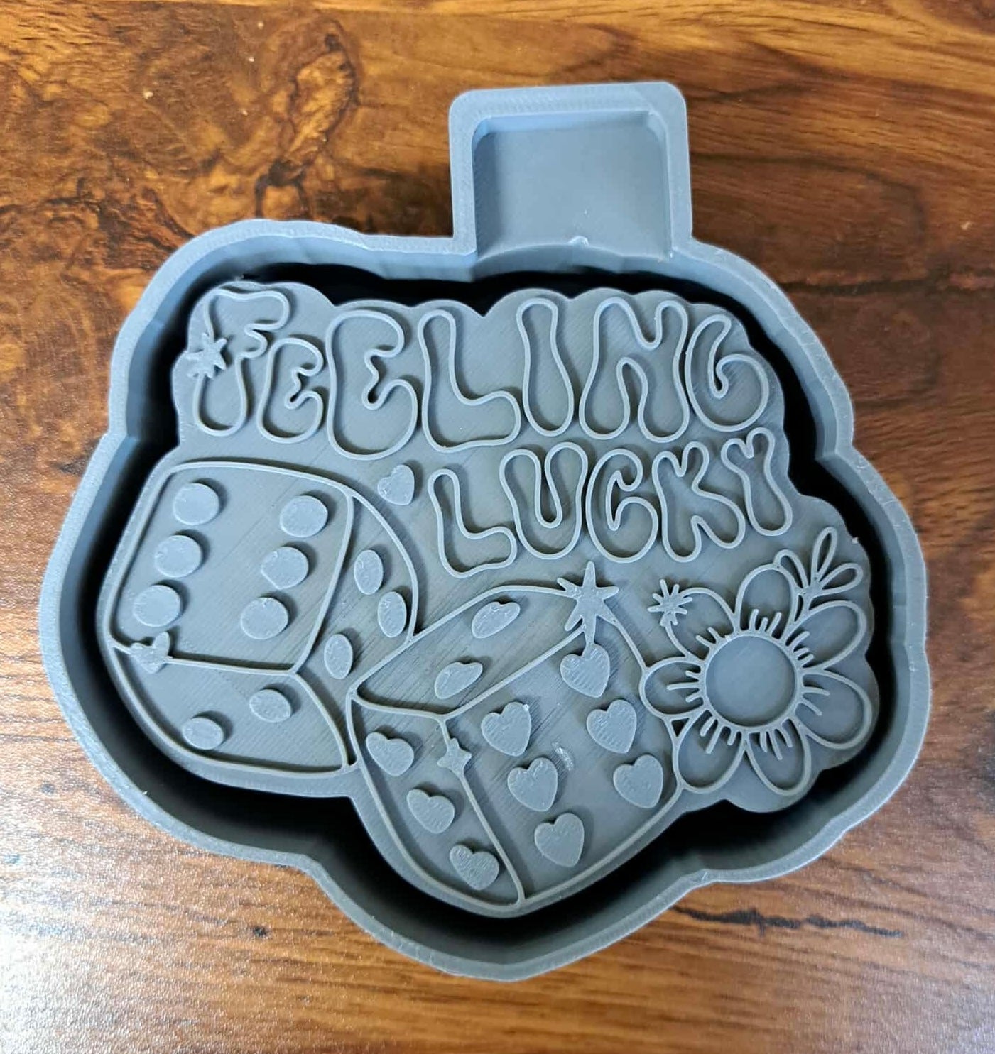 Gray 3D mold housing with 'Feeling Lucky' text and dice design on a wooden surface used for us to sell silicone molds