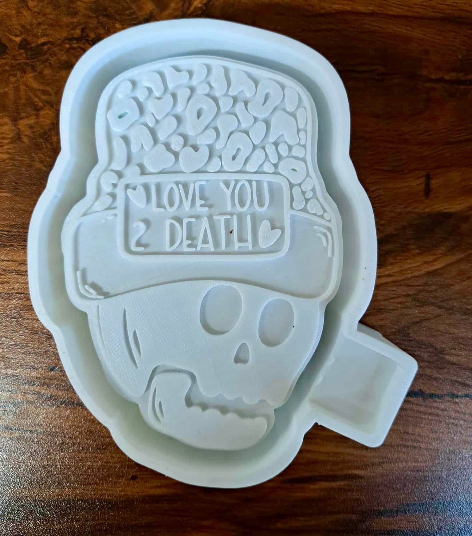 3D Housing shaped like a skull with a cap and text 'I Love You 2 Death' on a wooden surface to make silicone molds. 
