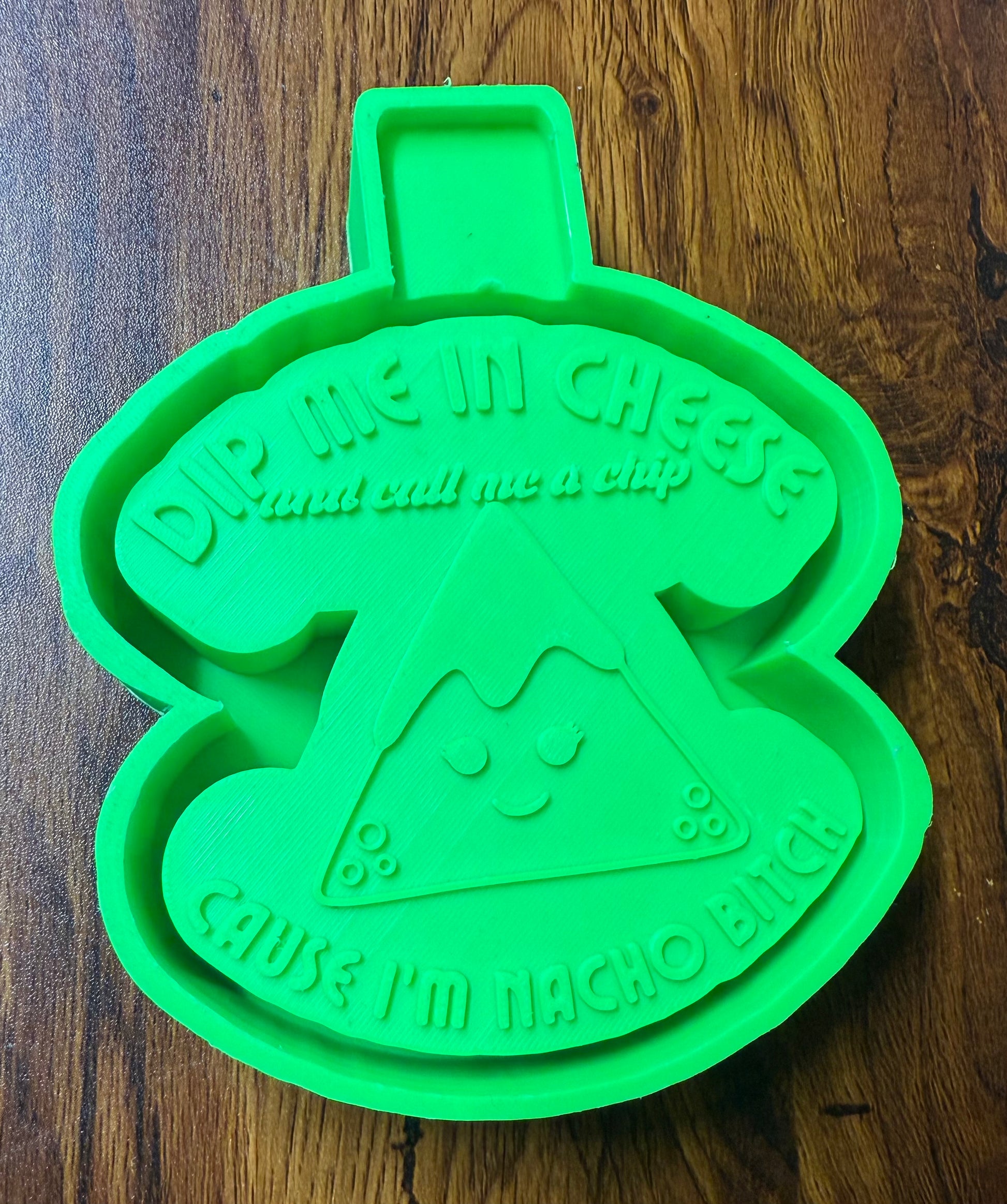 Green 3d housing shaped like a nacho chip with text on a wooden surface to be sold as a silicone mold
