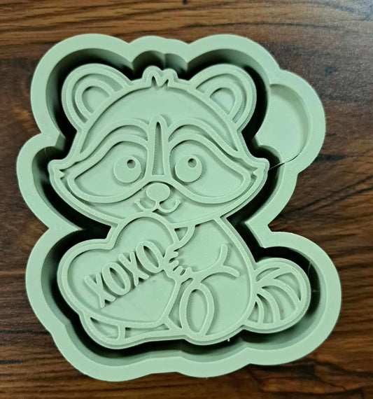 3d housing shaped like a raccoon with an xoxo heart on a wooden counter surface used to make silicone molds