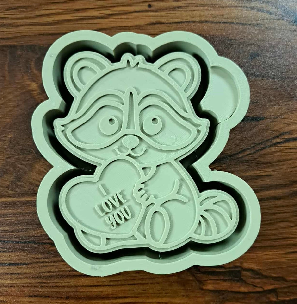 3d shaped mold housing like a raccoon holding a heart with 'I love you' text on a wooden counter surface for silicone mold. 